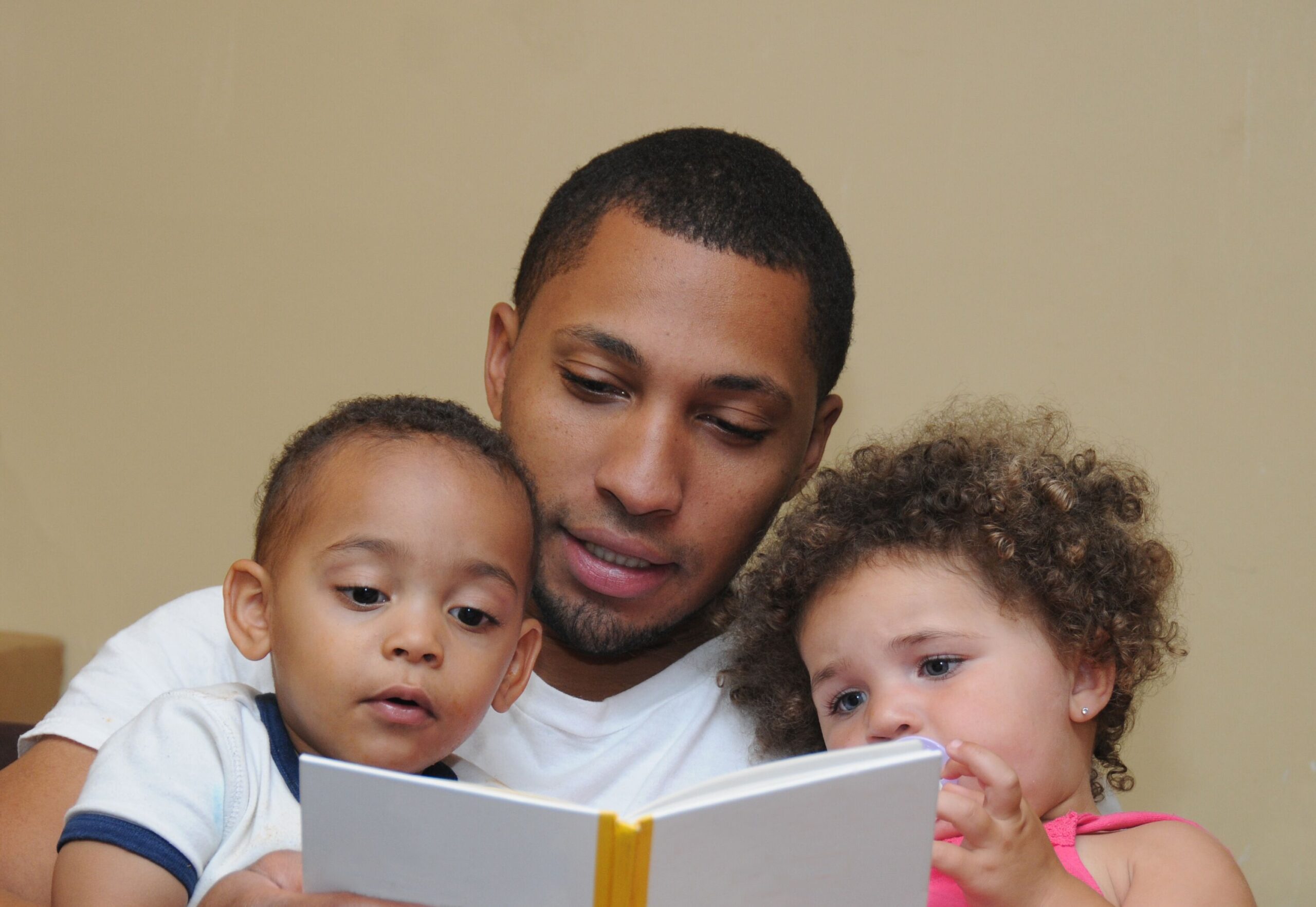 A man reads a book to two young children in a warm indoor setting.