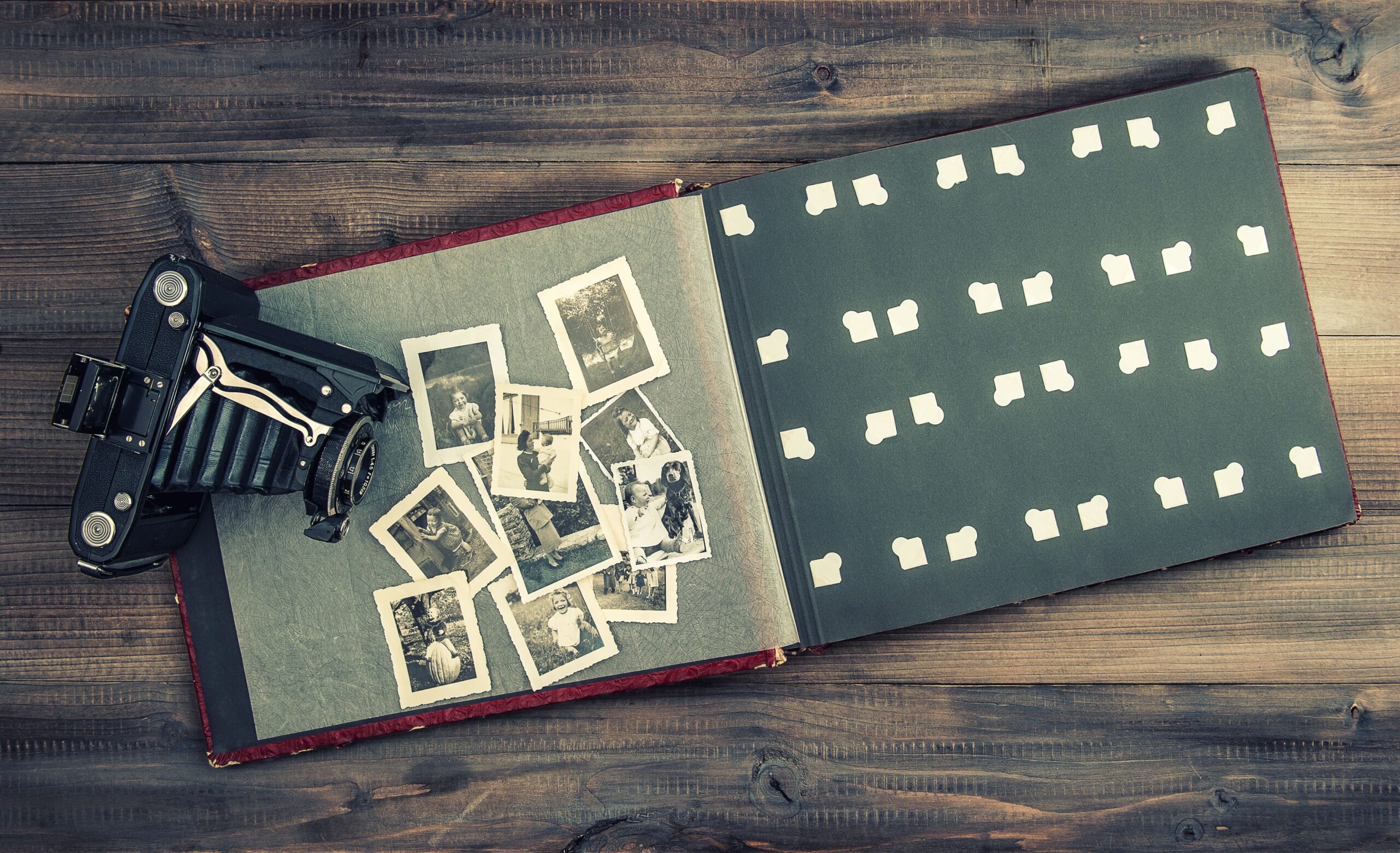 An open vintage photo album lies on a wooden table alongside an old-fashioned camera.