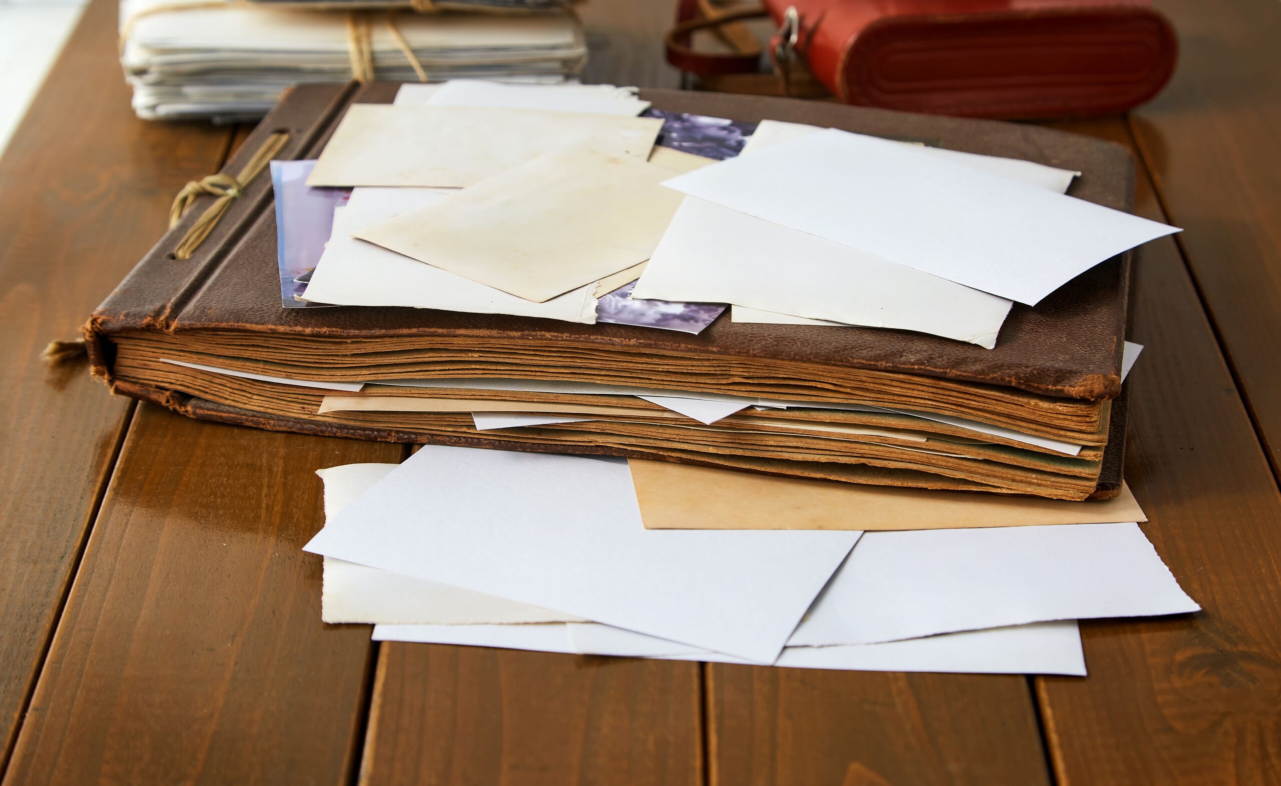 An old, worn photo album lays open on a wooden table, with scattered, faded photographs and blank papers