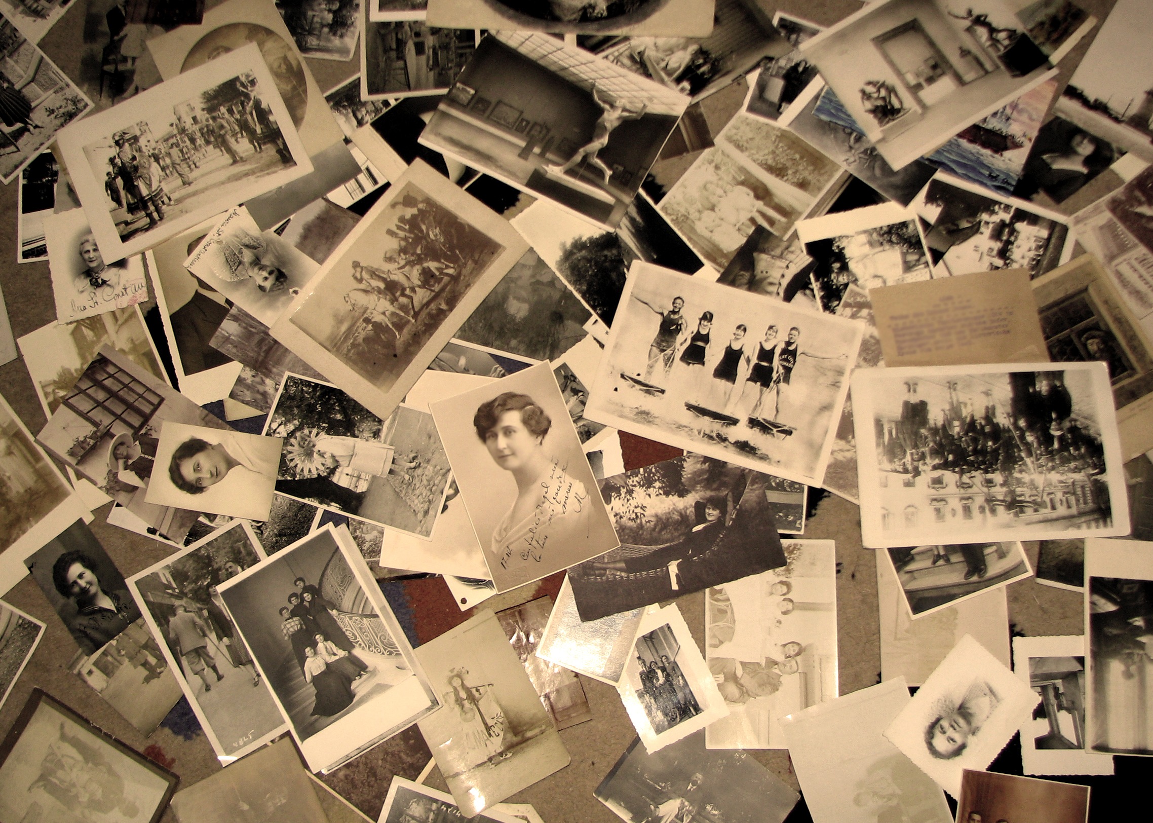 A collection of vintage black-and-white photographs sprawled across a surface, showing people and scenes from the early 20th century.